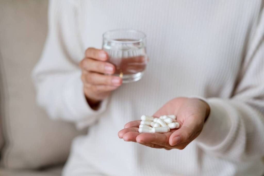 A woman holding white pills and a glass of water
